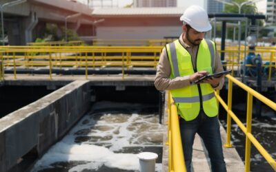 Employee in safety gear standing outside a wastewater treatment plant, looking frustrated and determined.