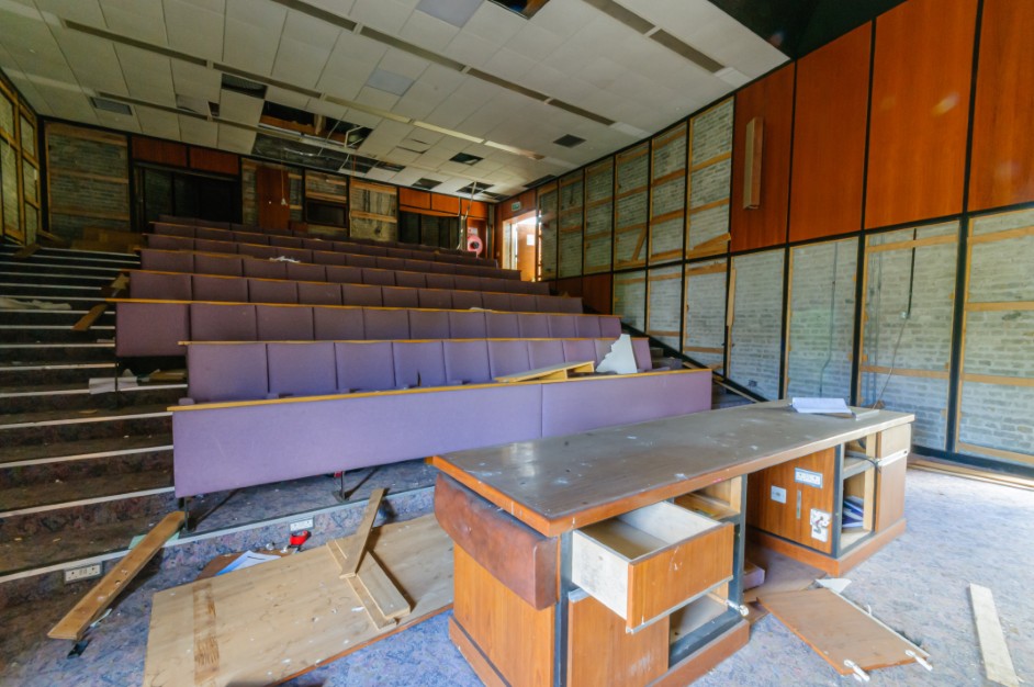 Empty lecture hall with overturned chair and scattered papers symbolizing professional chaos.