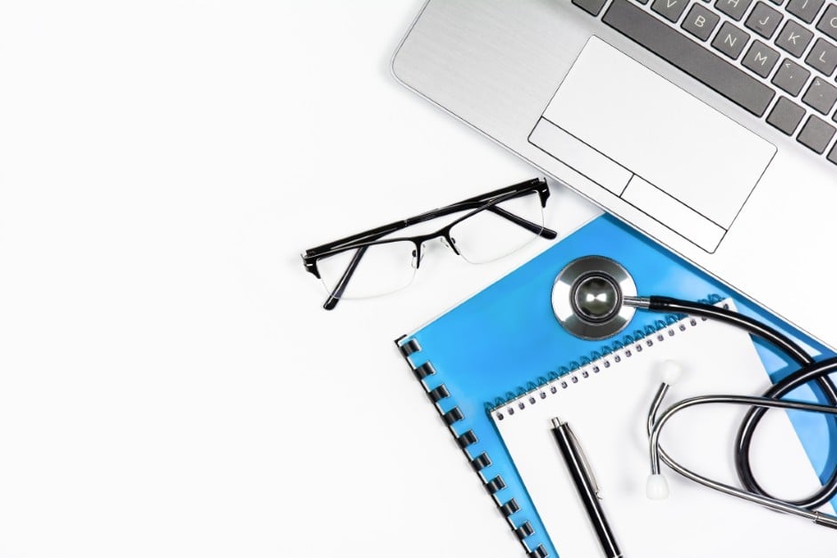 A closed laptop, a doctor’s note, and a pair of glasses on a desk symbolize a worker on medical leave.