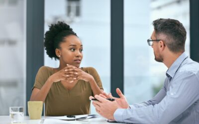 Employee sitting at a workplace table looking isolated during a tense discussion