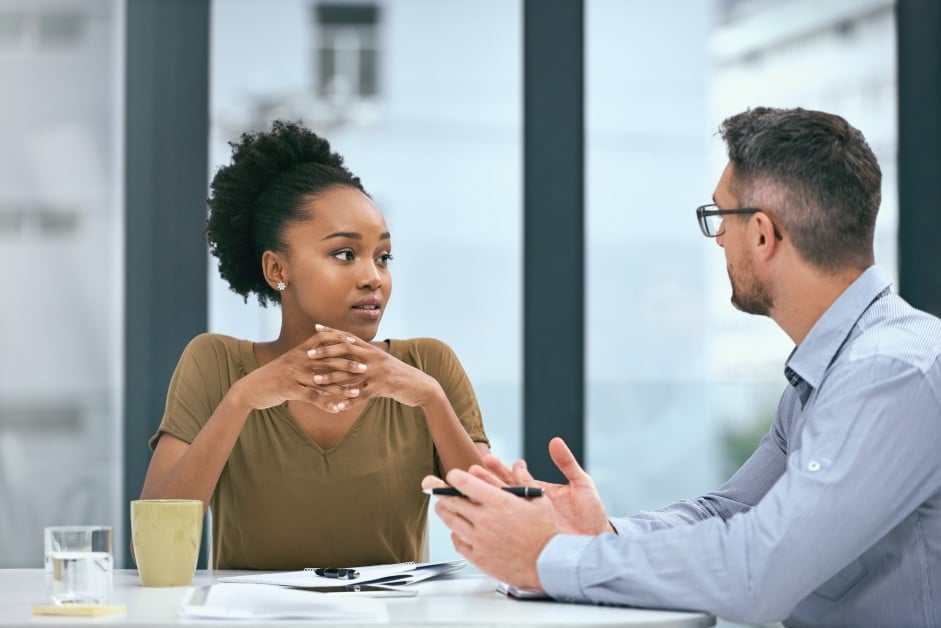 Employee sitting at a workplace table looking isolated during a tense discussion