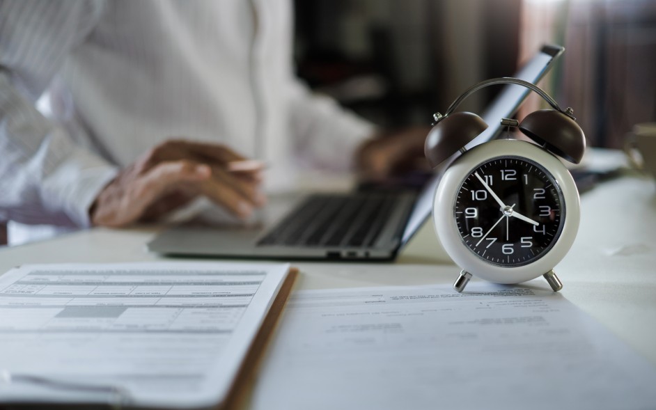 Employee reviewing paperwork with a worried look while a clock ticks in the background.