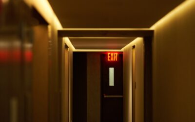 A dimly lit workplace hallway with one door slightly open, suggesting uncertainty after reporting discrimination.