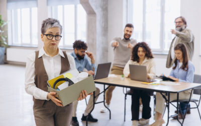 Employee standing alone at work while coworkers laugh and make racist comments nearby.