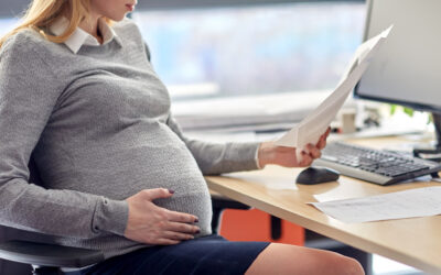 Pregnant employee reviewing workplace emails and notes at desk
