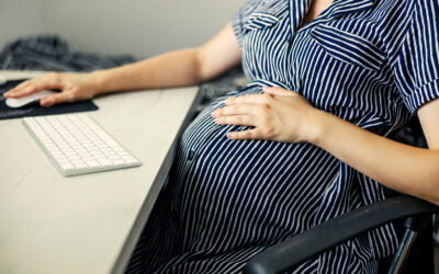 Pregnant employee at desk reviewing workplace emails, coworker complaints, FMLA paperwork, and termination documents.