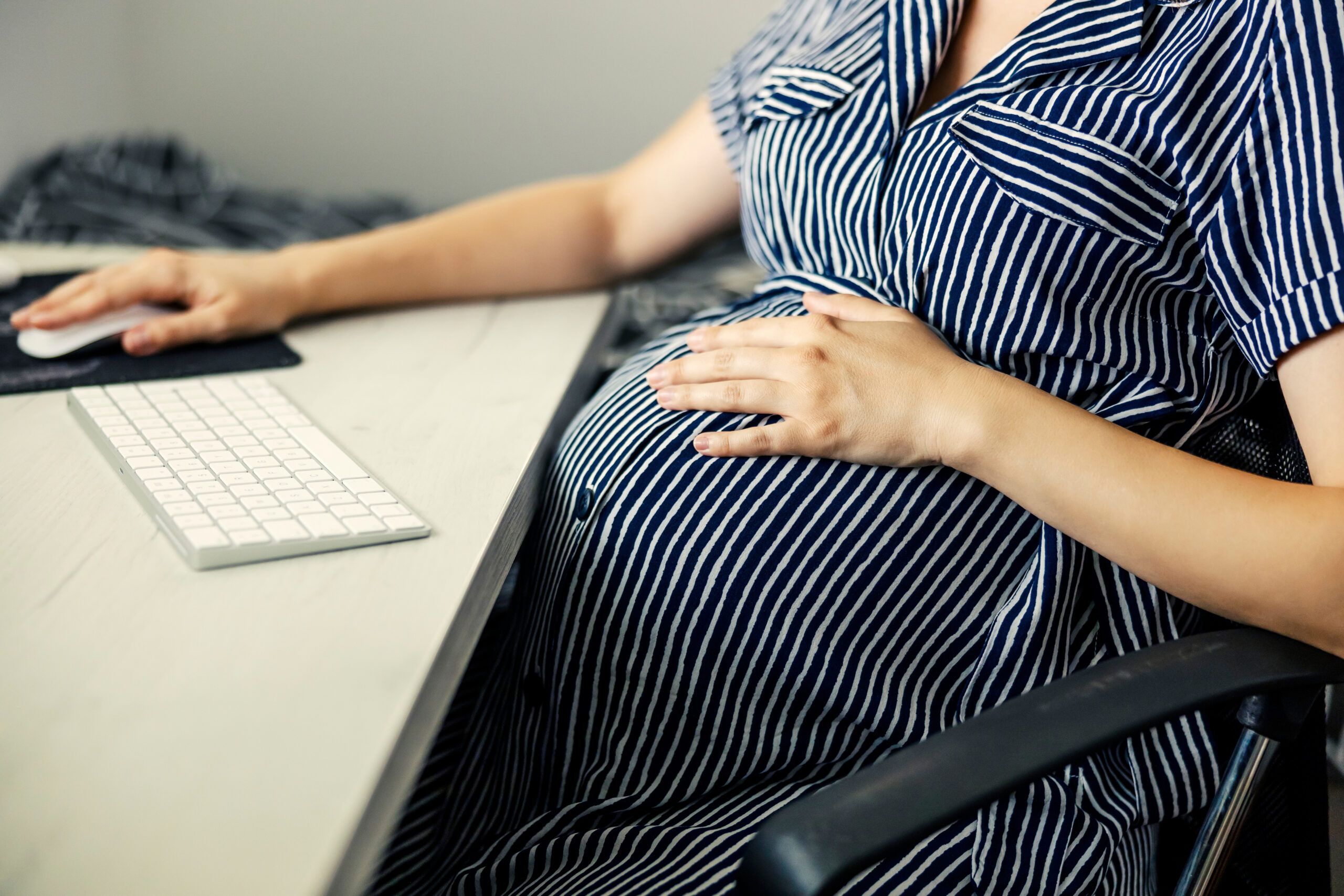 Pregnant employee at desk reviewing workplace emails, coworker complaints, FMLA paperwork, and termination documents.