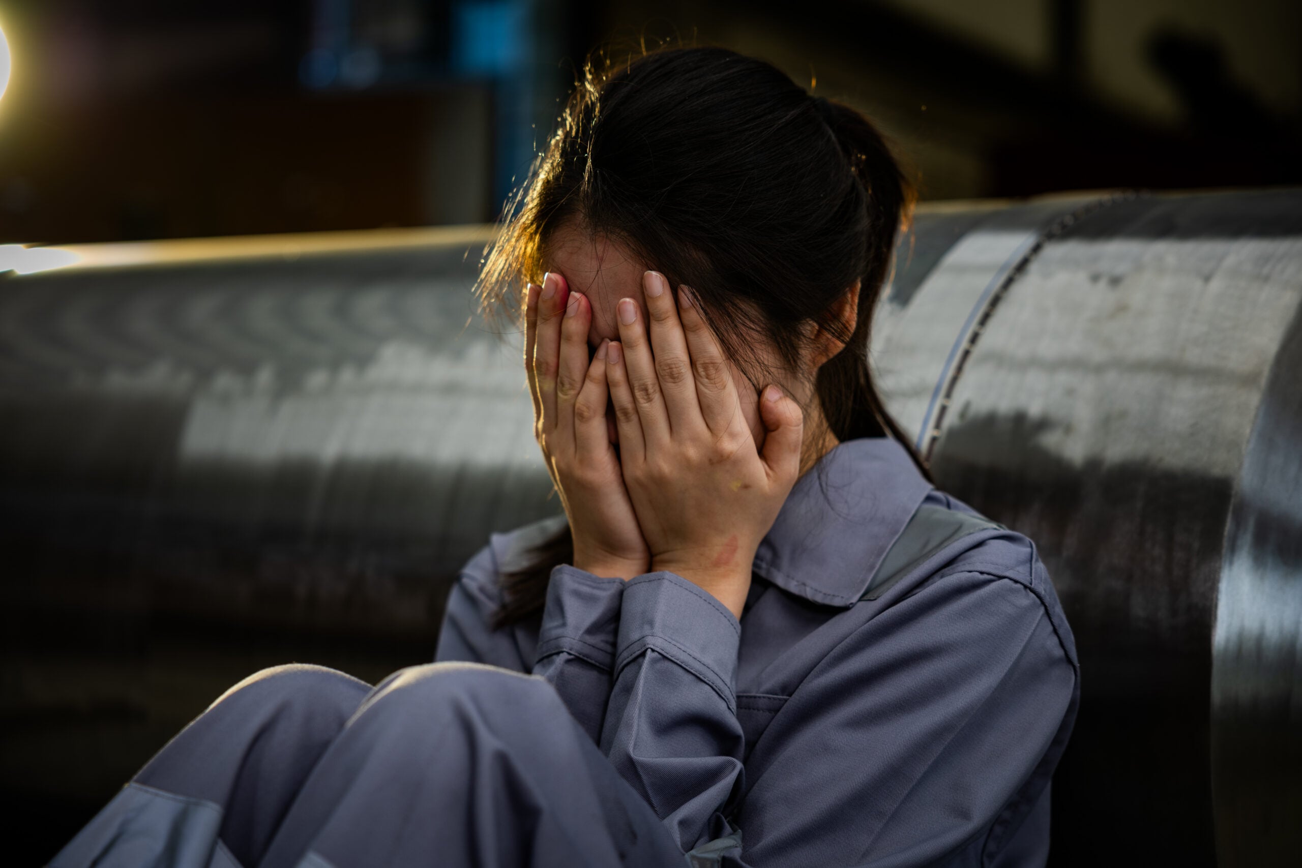 Employee sitting alone after repeated workplace sexual harassment while coworkers laugh in the background, illustrating a hostile work environment and emotional distress under Title VII.
